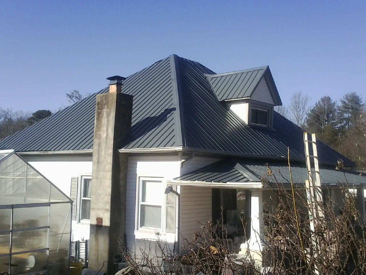 Dark blue standing seam metal roof on a white farmhouse with dormer — Slate & Tile Roof Repair by Roofing Brothers in Yutan