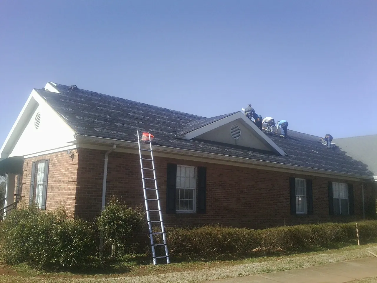 Crew tearing shingles off a brick ranch roof with a ladder set — Emergency Roof Repair work by our crew in Yutan