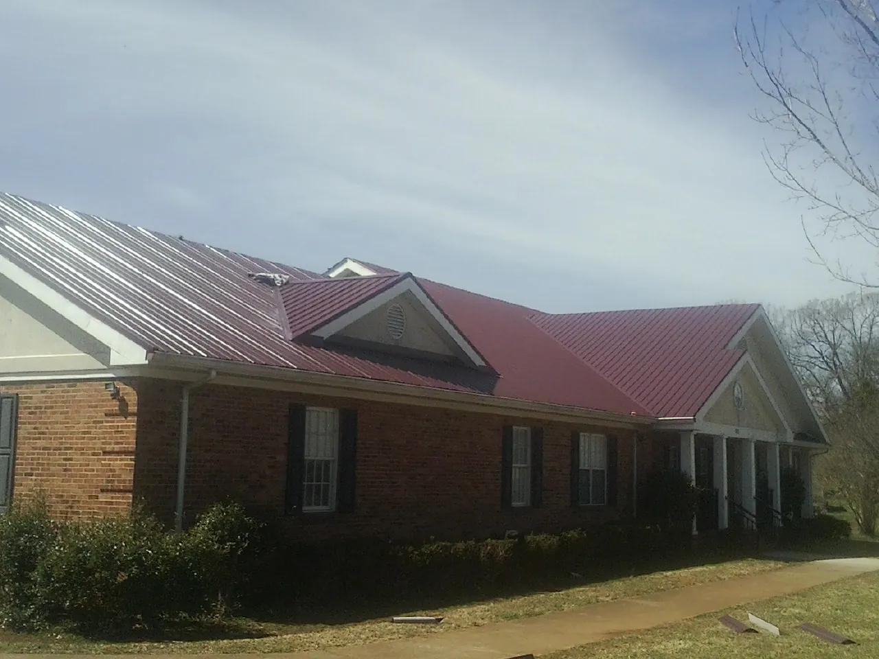 Red metal roof with gabled entries on a long brick building, from a Hail Damage Roof Repair job in Yutan