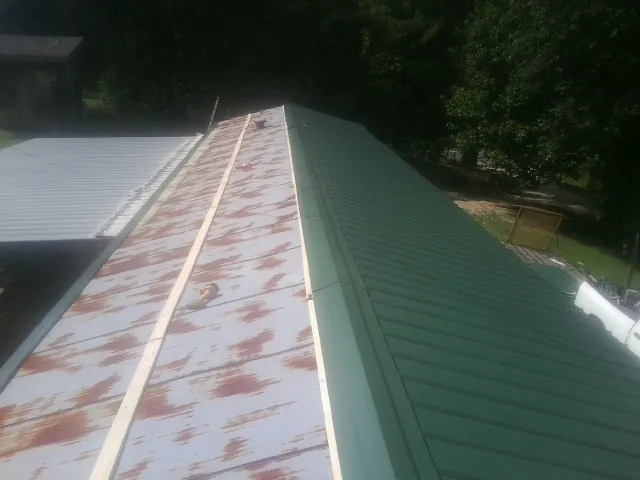 Old rusted panels beside newly installed green metal roofing — Wind Damage Roof Repair by Roofing Brothers in Yutan