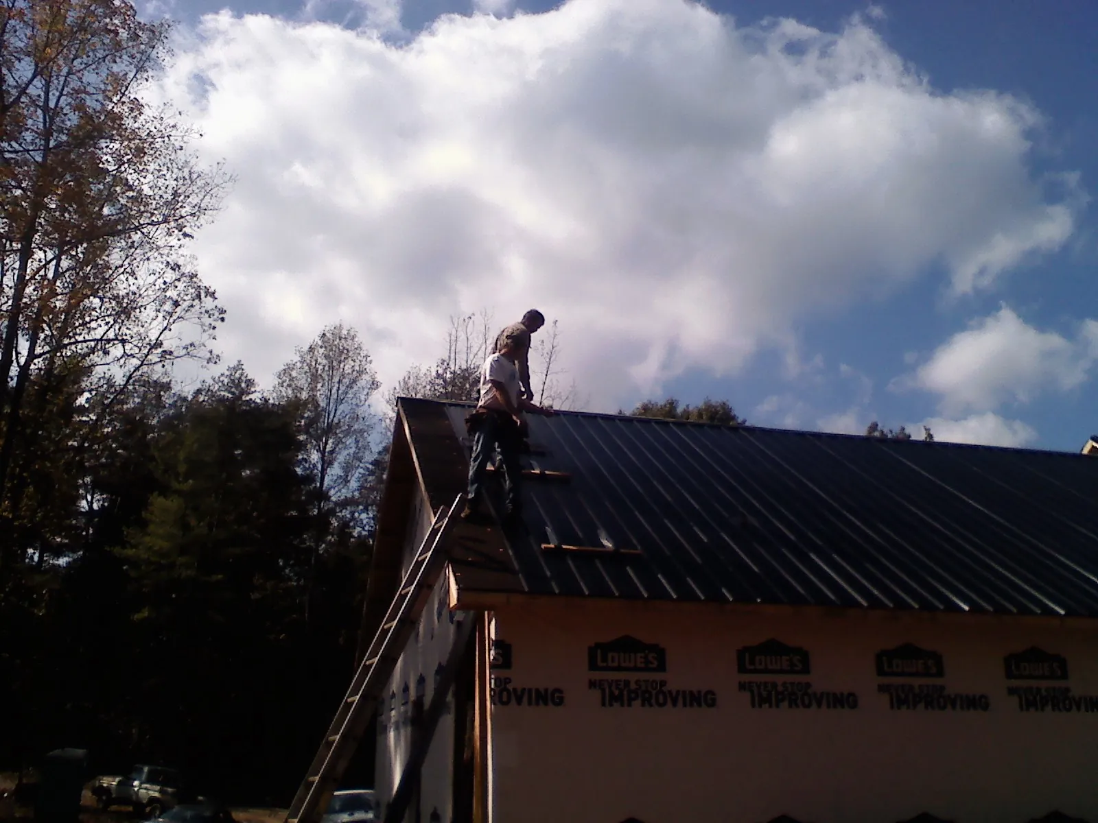 Roofer fastening dark metal panels high against a cloudy sky, from a Roof Inspection job in Yutan