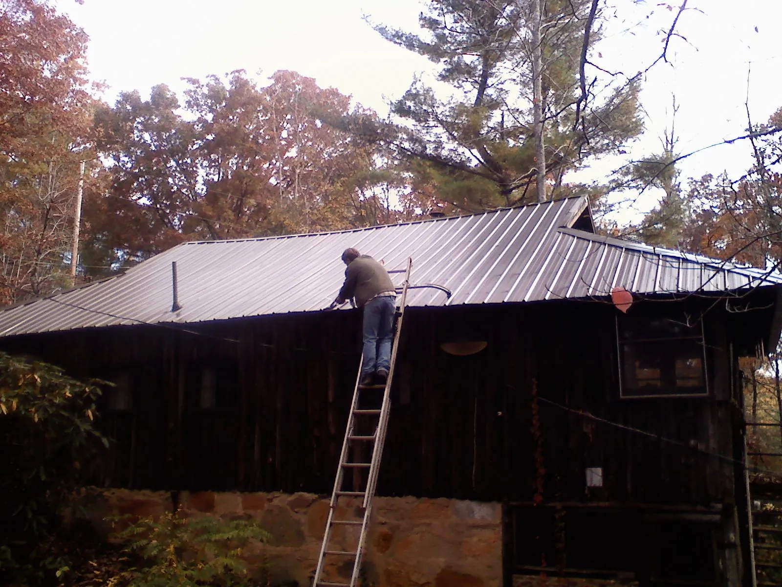 Roofer on a ladder working along the edge of a cabin metal roof in Yutan